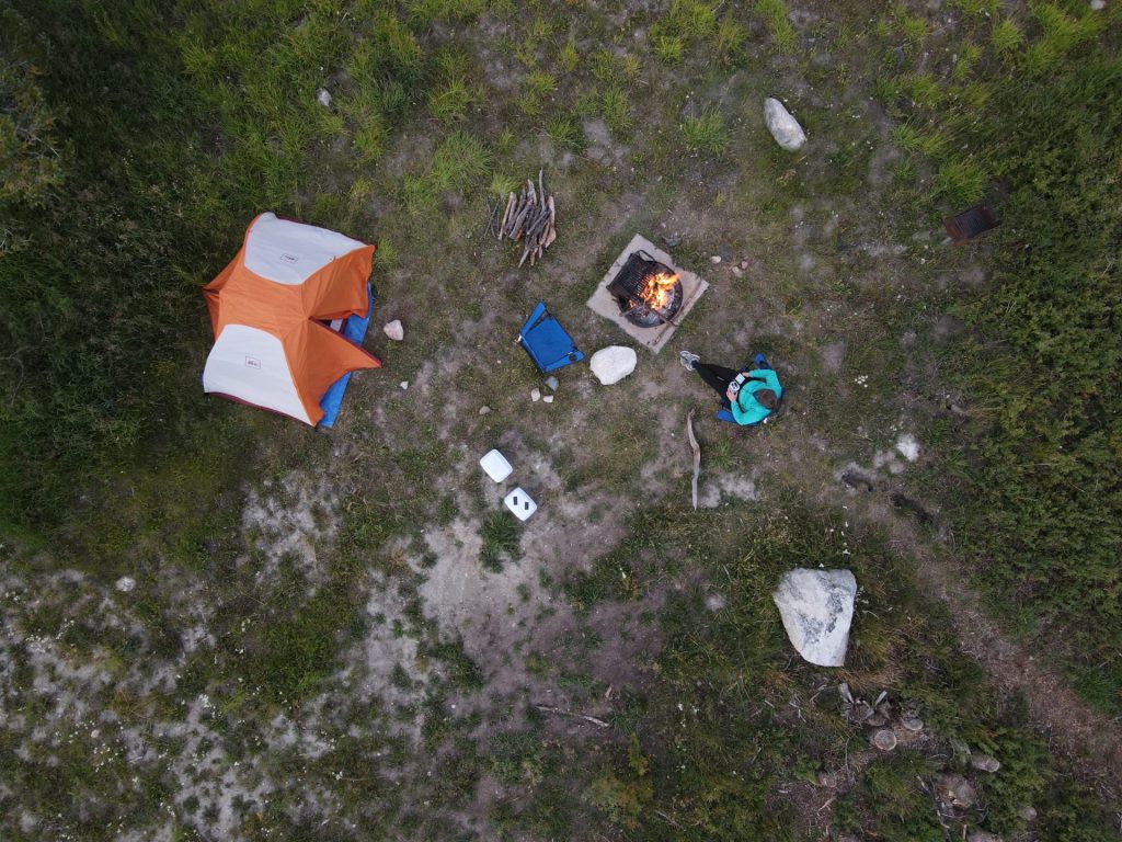 Aerial view of a tent, campfire, and person sitting in a chair reading.