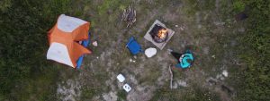 Aerial view of a tent, campfire, and person sitting in a chair reading.