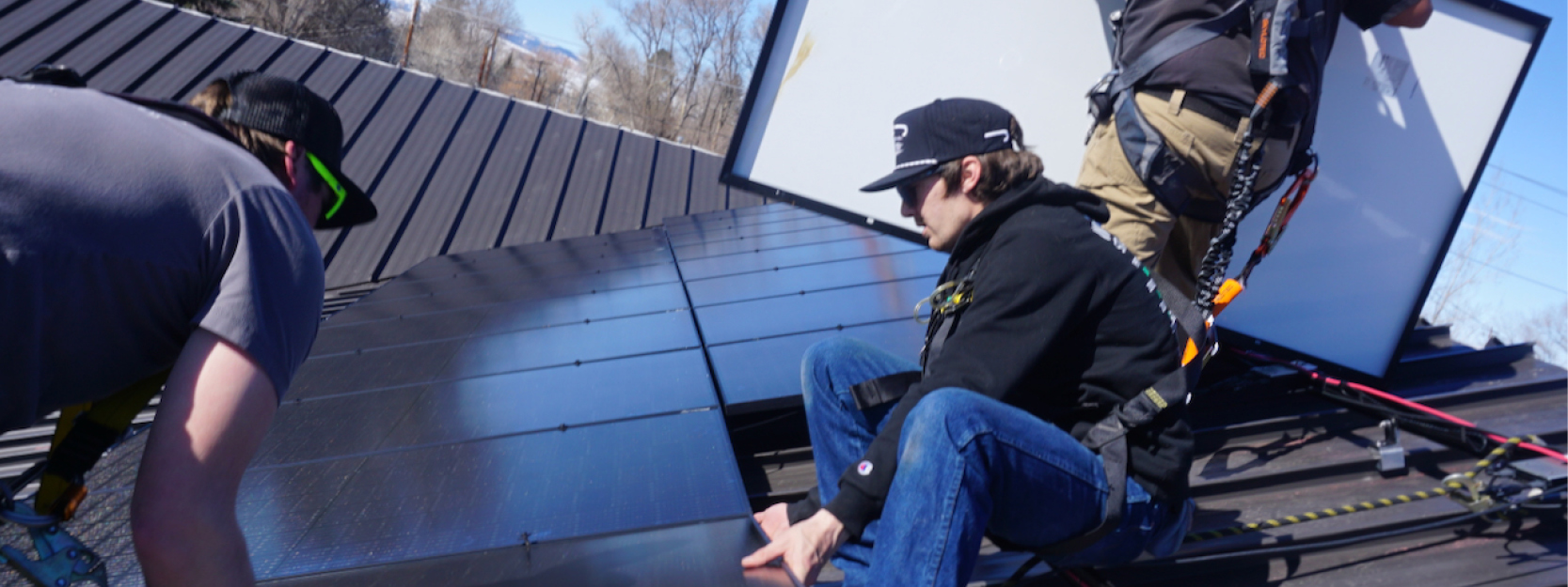 Three solar employees install a solar panel on a rooftop.