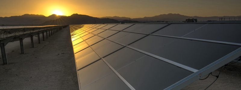 A closeup of a solar panel at a solar installation with the setting sun in the background