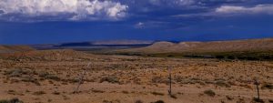 An expansive grassland landscape with fence in foreground and blue sky with clouds above